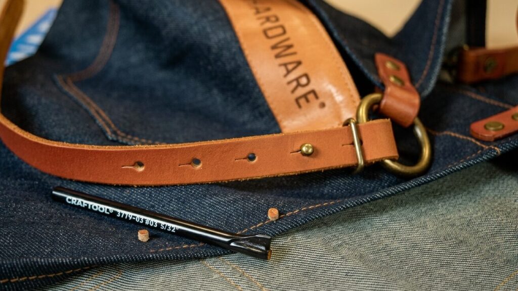 Lederriemen mit Knopflöchern für Sattlerknöpfe und Knopflochstanzer auf Jeansstoff